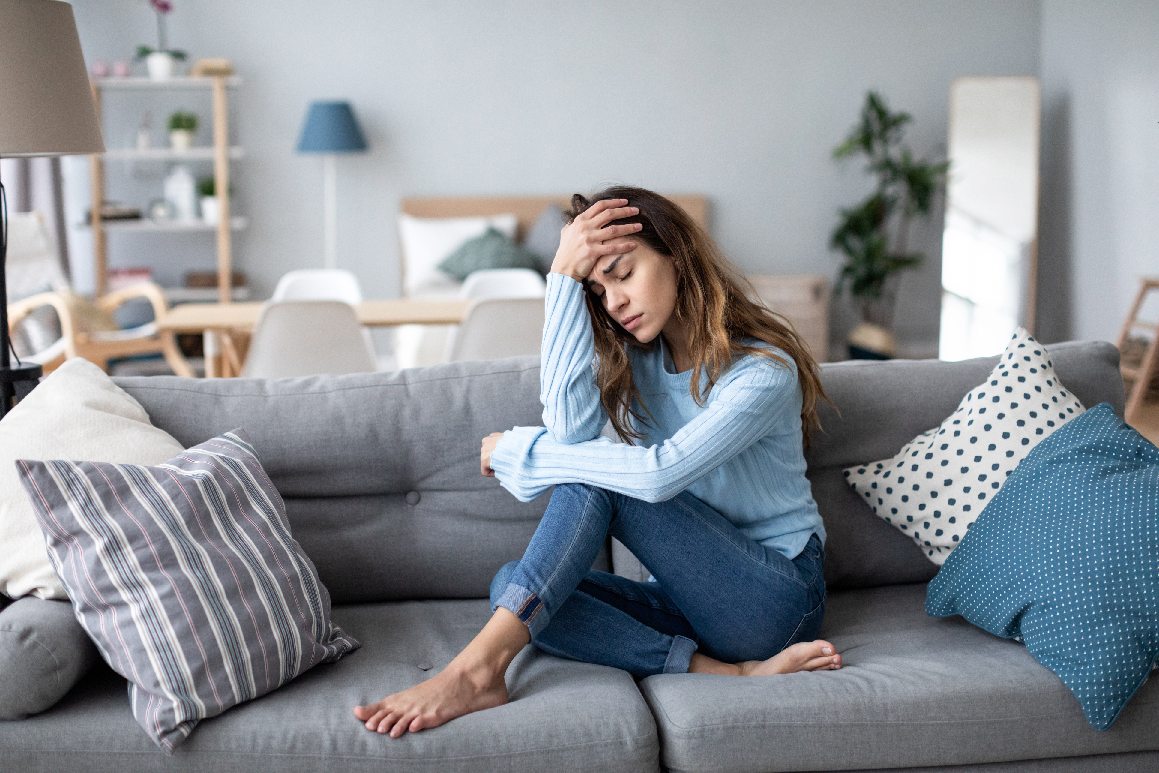 Sad upset woman sits on the sofa in the living room alone at home