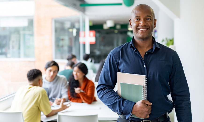 Profesor de pie sonriendo y sosteniendo unos cuadernos